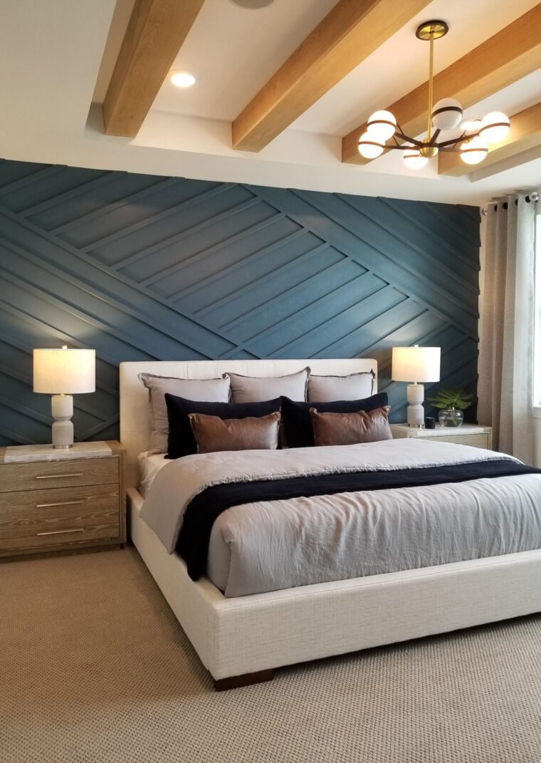 A modern-style bedroom with an abstract blue wall behind the bed’s headboard. The bed has gray, black and brown coloring and there are two nightstands on either side of the bed.